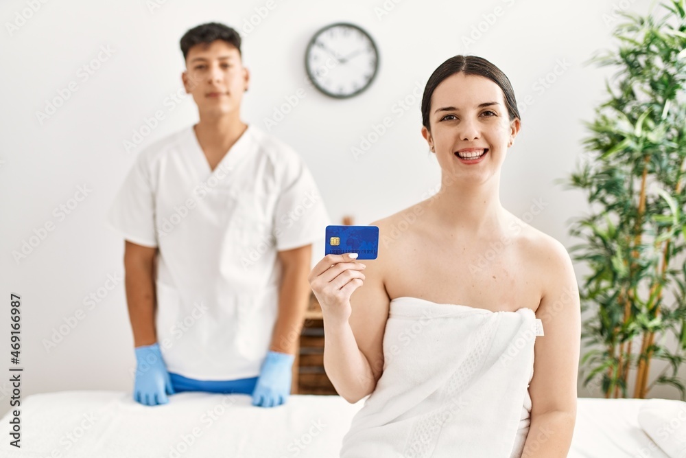 Fototapeta premium Woman smiling happy waiting to recive massage holding credit card at beauty center.