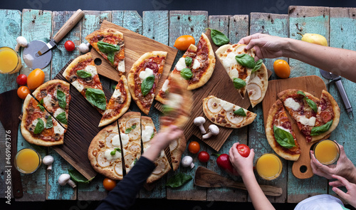 Children hands grab fresh pizza slices on oak cutting boards