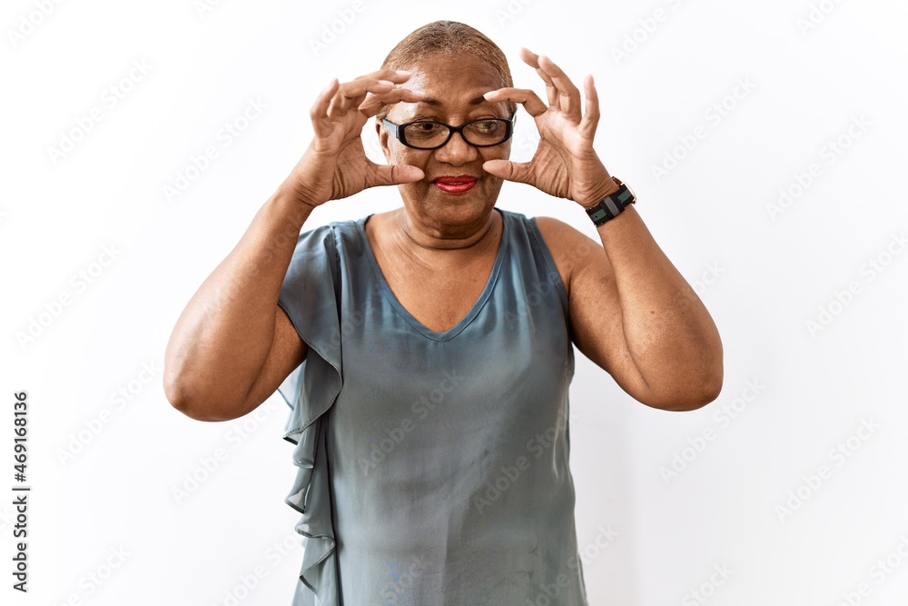 Mature hispanic woman wearing glasses standing over isolated background trying to open eyes with fingers, sleepy and tired for morning fatigue Mature hispanic woman wearing glasses standing over isolated background trying to open eyes with fingers, sleepy and tired for morning fatigue