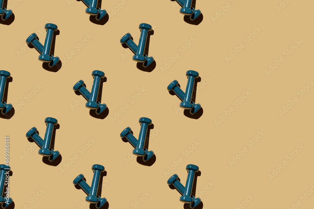 Blue fitness dumbbells on a beige background, pattern, top view, crust criss-cross together. Copy space.