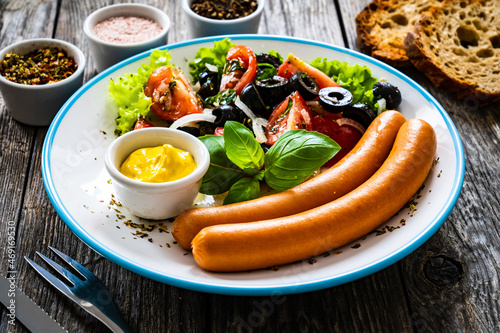 Breakfast - boiled sausages, bread and fresh vegetables served on wooden table 