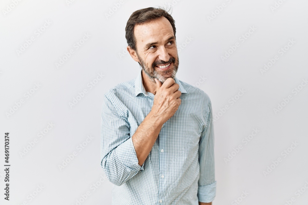 Middle age hispanic man with beard standing over isolated background with hand on chin thinking about question, pensive expression. smiling and thoughtful face. doubt concept.