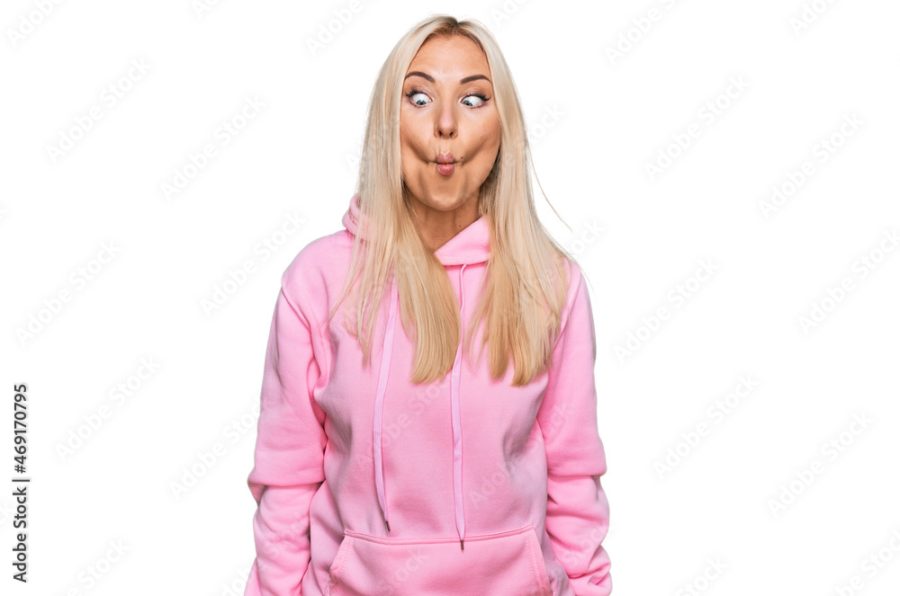 Young blonde woman wearing casual sweatshirt making fish face with lips, crazy and comical gesture. funny expression. Young blonde woman wearing casual sweatshirt making fish face with lips, crazy and comical gesture. funny expression.