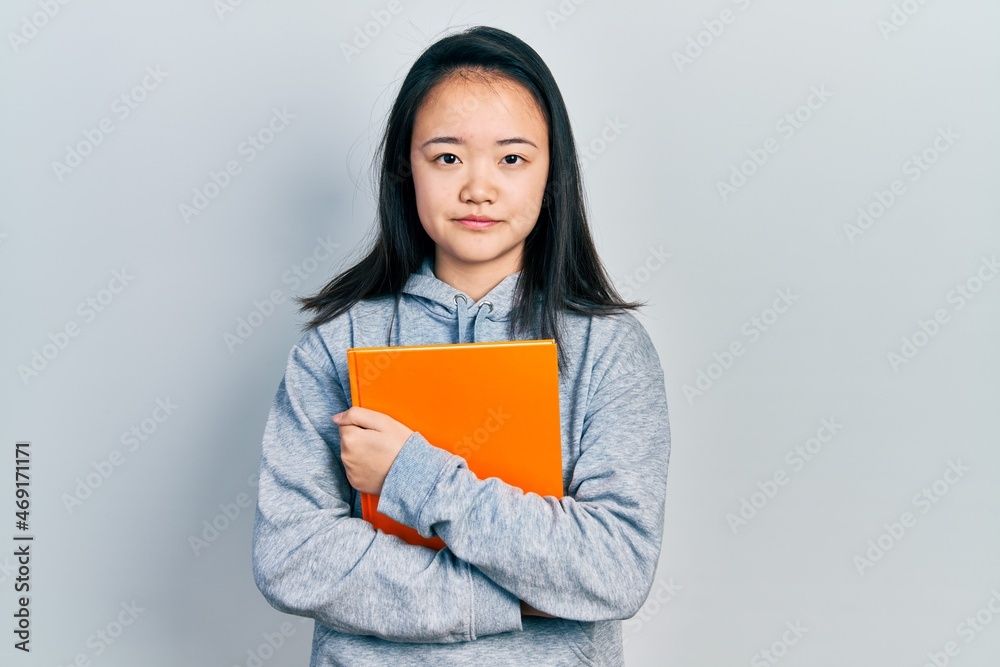 Young chinese girl holding book relaxed with serious expression on face. simple and natural looking at the camera. Young chinese girl holding book relaxed with serious expression on face. simple and natural looking at the camera.