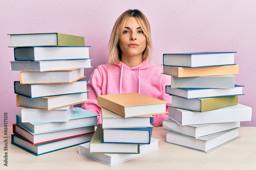 Young caucasian woman sitting on the table with books relaxed with serious expression on face. simple and natural looking at the camera. Young caucasian woman sitting on the table with books relaxed with serious expression on face. simple and natural looking at the camera.