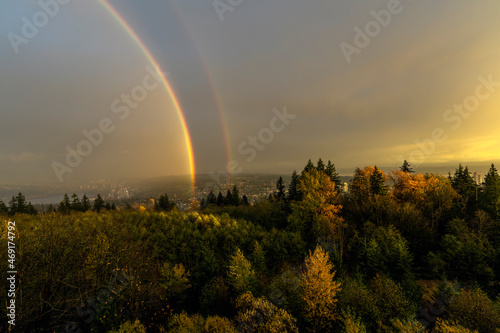 Double rainbow over Fraser Valley against dark rainclouds on a misty day as seen from Burnaby Mountain  BC.