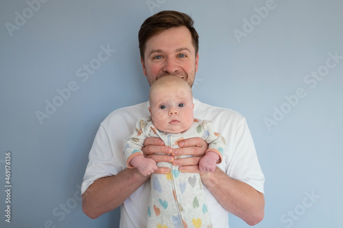 Young man holding a 3months old baby, isolated on blue background photo