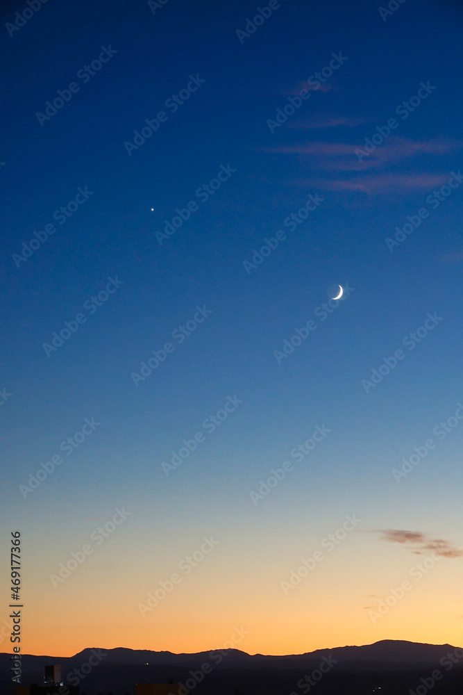 Vertical photo of dusk with the moon and venus in the sky and the silhouette of mountains on the horizon