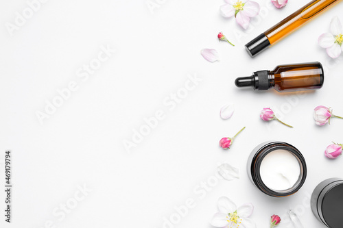 Spring concept of natural organic cosmetics. Clean brown glass cosmetic bottles with dropper, cream, delicate spring flowers on white background flat lay top view. Beauty herbal product spa aroma oil