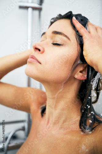 Woman enjojing the shower at her bathroom. Lady washing her hair and bodu under the shower.