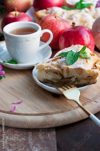 Apple homemade pie with red apples, mint and fork on wooden board on brown background. Rustic style