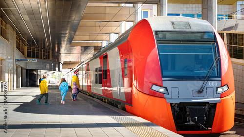 Boarding passengers in the carriage of the electric train. The train is on the platform of the railway station. Traveling with children by public transport. Mom and children enter the train carriage.