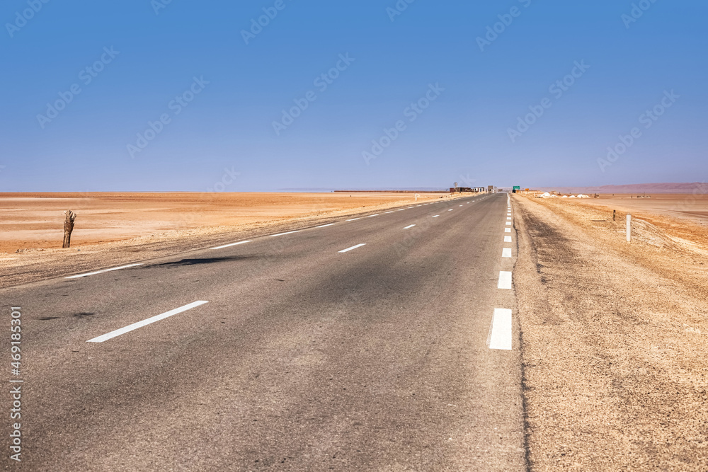 Fototapeta premium An asphalt road that runs along the Sahara Desert. Sahara Desert, Tunisia