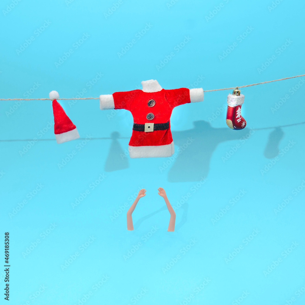 Santa Claus blouse, red hat with white pompom and a red shoe hanging on a rope. Women's arms below. Pastel blue background. Surreal Christmas or New Year's eve party invitation.  Design for card.