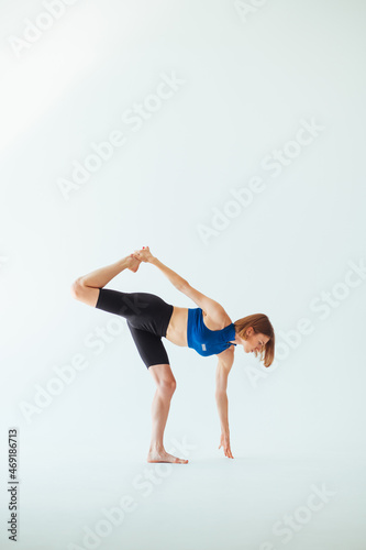 Athletic attractive woman in a top is training on a white background, doing leg stretches and looking down at the ground.