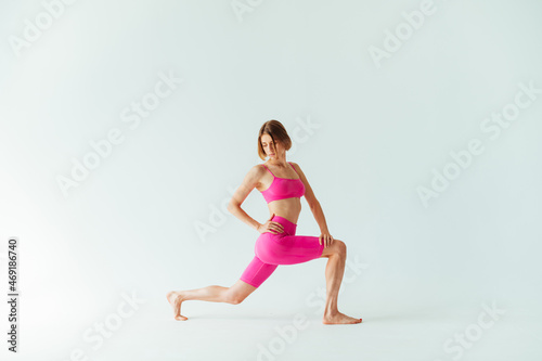 Athletic woman in pink clothes for training stands on a white background and stretches up.