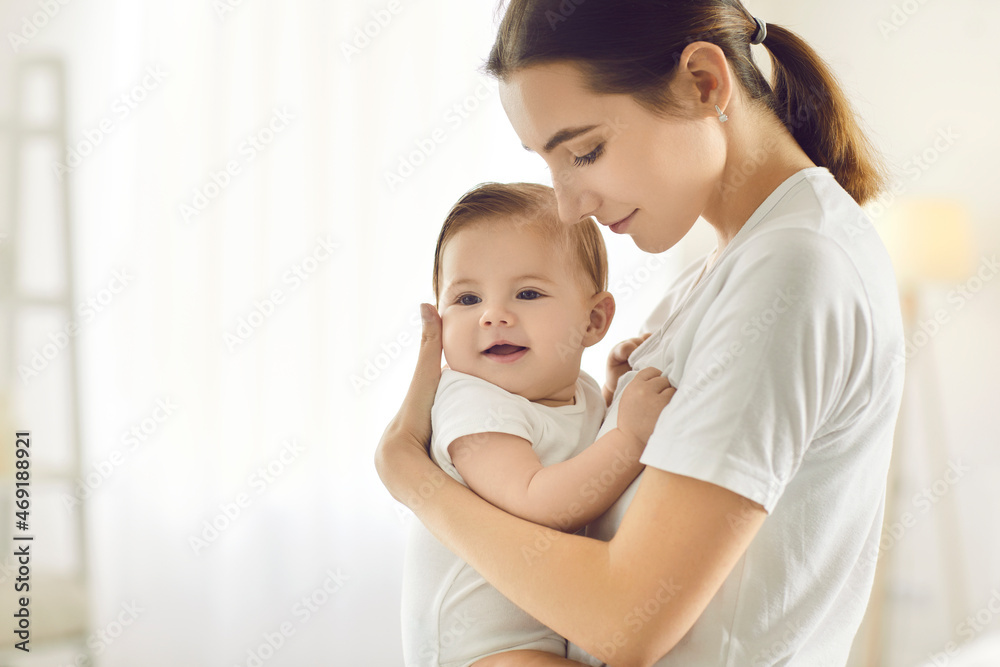 Portrait of happy beautiful young mom holding cute sweet little baby in her arms. White copy space background. Family, mother's tender embrace, maternal bond, love, care, nurture of children concepts Portrait of happy beautiful young mom holding cute sweet little baby in her arms. White copy space background. Family, mother's tender embrace, maternal bond, love, care, nurture of children concepts