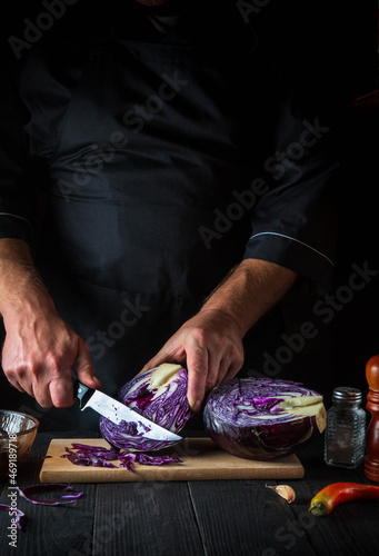 The cook is cutting red cabbage with a knife. Cooking vegetable salad in the restaurant kitchen. Vegetable diet idea.