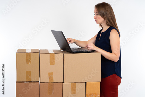 Woman entrepreneur. Businesswoman with cardboard boxes. She is typing something on her laptop. Small business owner concept. Boxes as fulfillment metaphor. Entrepreneur is processing orders