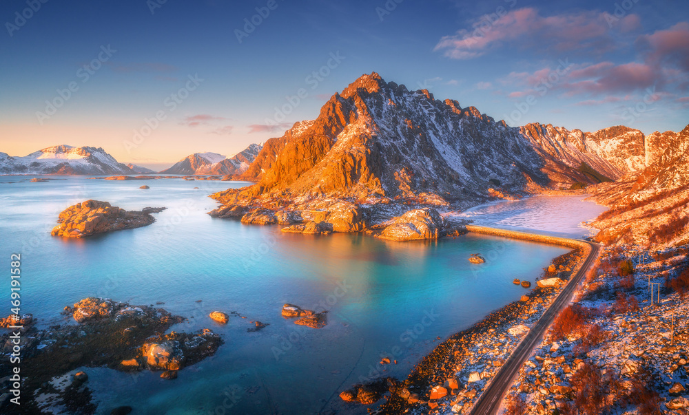 Aerial view of beautiful mountains, small islands in the sea, road, blue sky at sunset in Lofoten islands, Norway in winter. Top view of road, snowy rocks, stones, sea coast, clear water. Top view - obrazy, fototapety, plakaty 