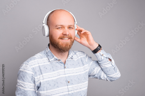 Bearded hipster man listening music at white headphones.