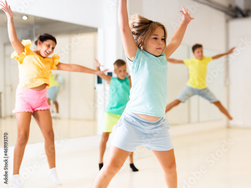 Happy cute sporty tween girl exercising in modern choreographic studio, jumping together with group of children.