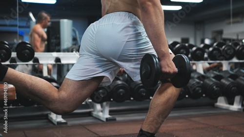 A young man squats with kettlebells for pumping the buttocks.