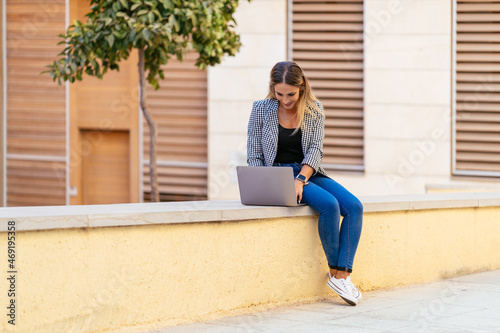 Smiling freelancer browsing laptop in street