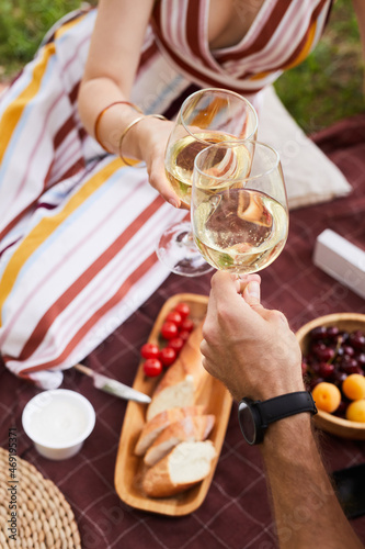 Vertical close up of young couple holding wine glasses while enjoying romantic picnic outdoors, copy space