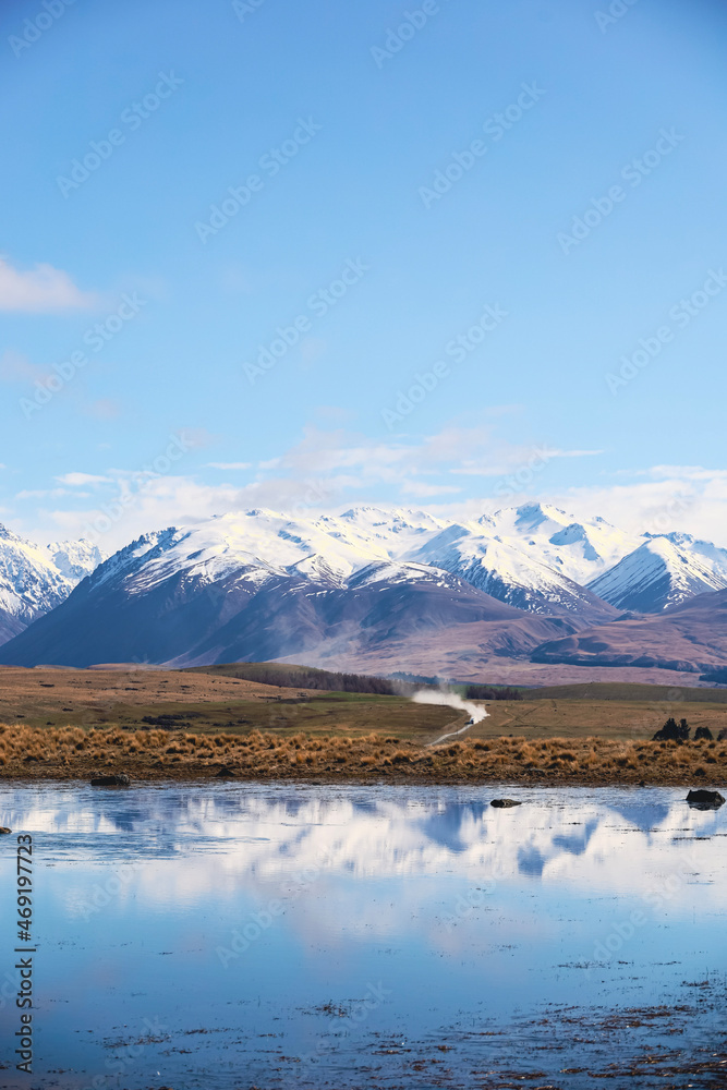 Snow top mountains reflect in lake and blue sky