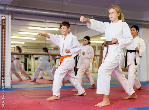 Young boys and girls performing kata moves with their trainer in gym during karate training.