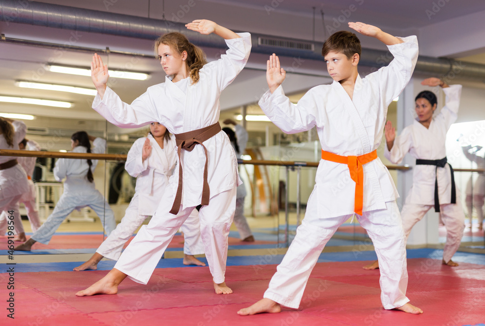 Kids in karate uniform exercising kata during group training with trainer.