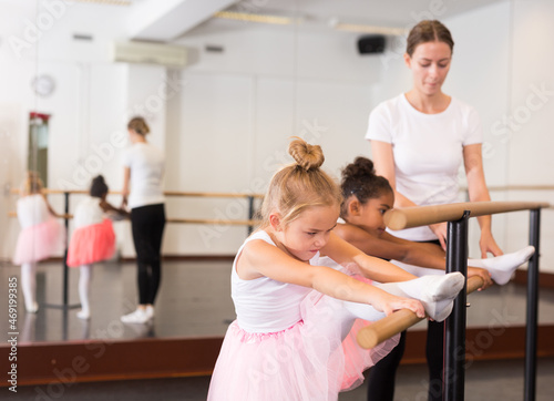 Female ballet trainer teaching two little girls near ballet barre in dancing hall