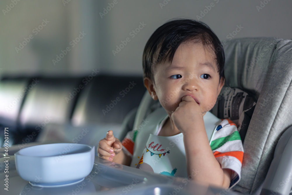 Adorable joyful and Happy 1years old Chinese baby boy having food while sit on baby chair Adorable joyful and Happy 1years old Chinese baby boy having food while sit on baby chair