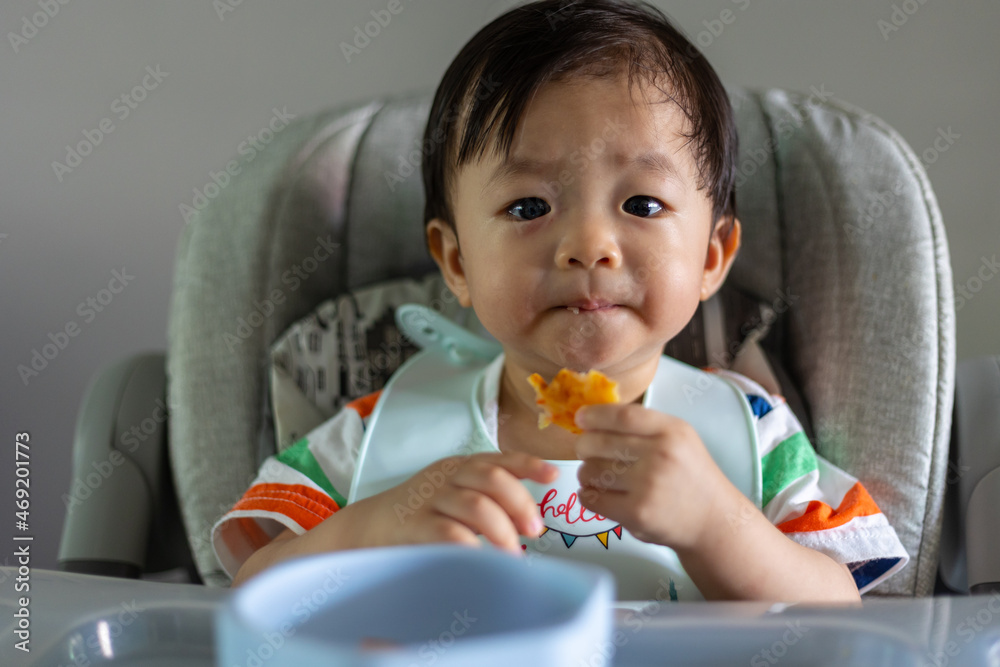 Adorable joyful and Happy 1years old Chinese baby boy having food while sit on baby chair Adorable joyful and Happy 1years old Chinese baby boy having food while sit on baby chair