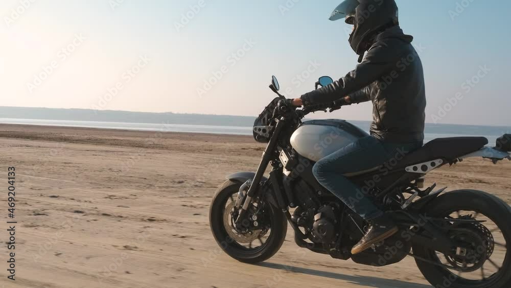 Motorcyclist driving his customized fast motorbike on the dirt road in desert around sea or lake