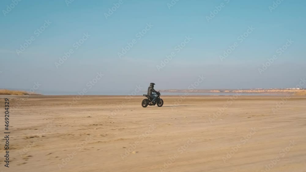 Motorcyclist driving his customized fast motorbike on the dirt road in desert around sea or lake Motorcyclist driving his customized fast motorbike on the dirt road in desert around sea or lake