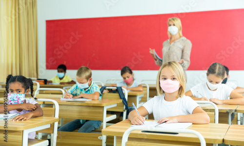 Young girl in protective mask is sitting at the desk in the classroom
