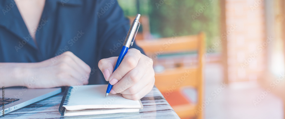 Woman hand writing on a notepad with a pen and use a laptop computer in the office.