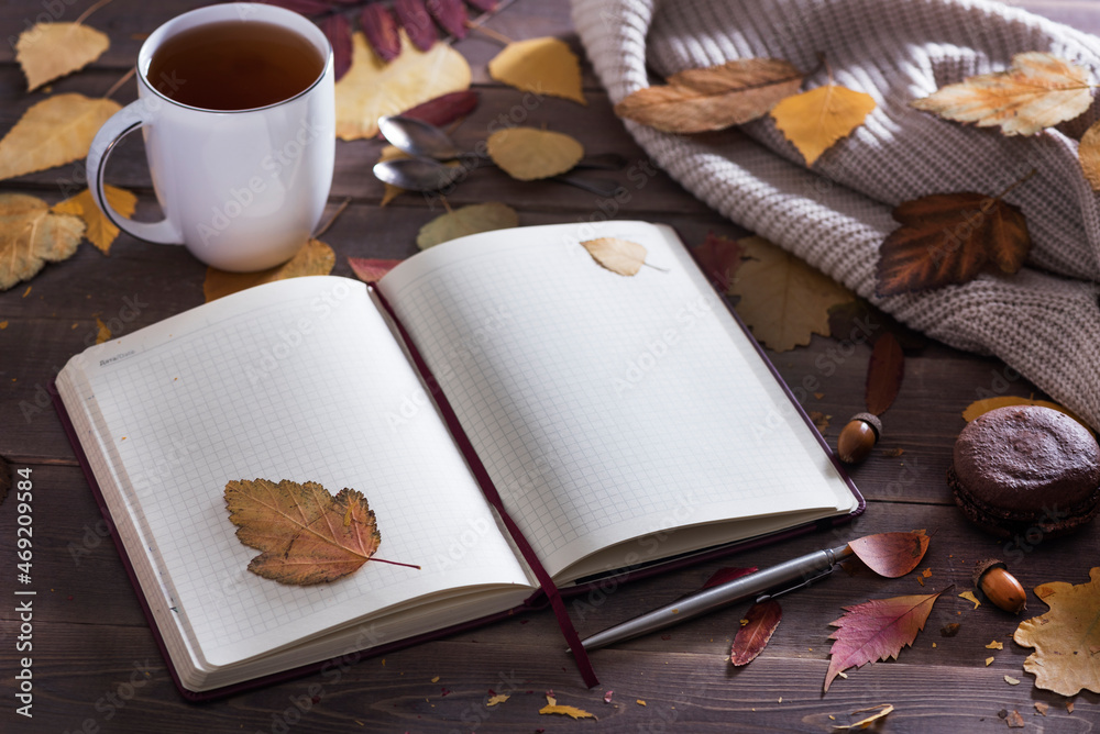 Autumn season concept, beautiful autumn composition with notebook, tea сup, autumn leaves, chocolate macoroon on rustic wooden table, natural background.