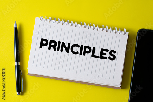PRINCIPLES written in a notebook on yellow background with pen and smartphone.