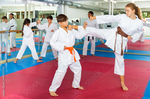 Young girl and boy in kimono training kicks during group karate training.