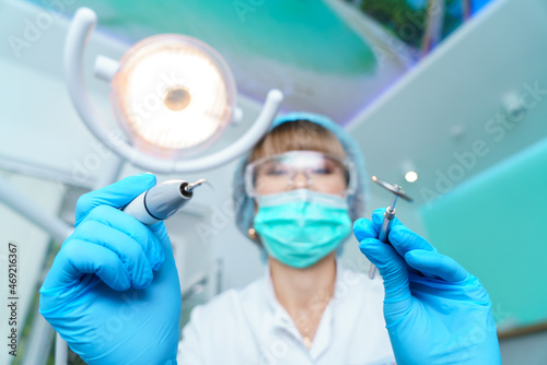 Dentist in a surgical mask  holding an angle mirror and a drill  ready to work. Woman dentist at work. Makes an examination and treatment of teeth for caries.