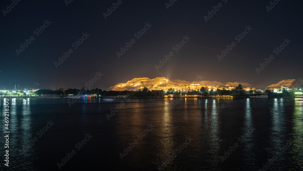 A night in Egypt. Glowing ships are visible on the calm surface of the Nile. Reflection. Picturesquely illuminated sand dunes rise against the dark sky.