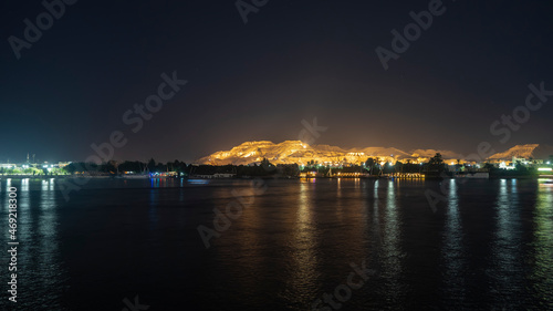 A night in Egypt. Glowing ships are visible on the calm surface of the Nile. Reflection. Picturesquely illuminated sand dunes rise against the dark sky.