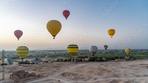 Colorful balloons rise into the morning sky over Luxor. Below you can see the sandy desert, archaeological excavations. In the distance is the green valley of the Nile. Egypt