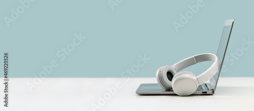 Laptop. Mockup screen and wireless headphones on white desk. plain blue background. Distant learning. working from home, online courses. minimal. Helpdesk support or call center headset photo