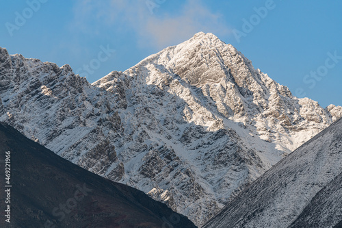 Snow capped mountain peaks in northern Canada with misty, foggy clouds covering the peaks with white, winter theme and spectacular blue sky behind. 