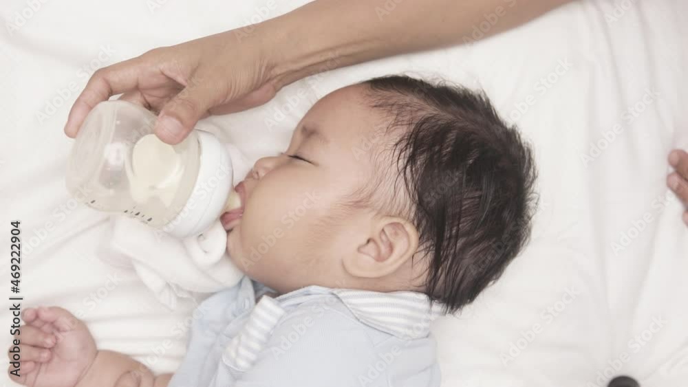 Baby Boy Drinking Milk From Feeding Bottle Held By His Mother In The Bed. - high angle Baby Boy Drinking Milk From Feeding Bottle Held By His Mother In The Bed. - high angle