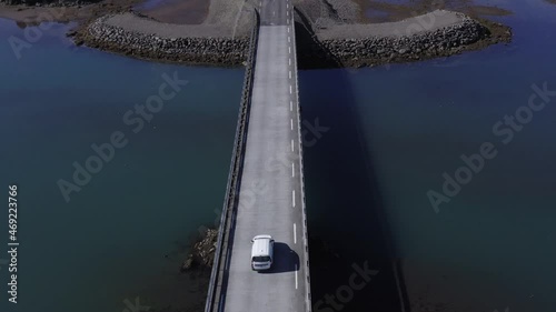 White car crossing bridge over calm river mouth at Iceland coastal land, aerial photo